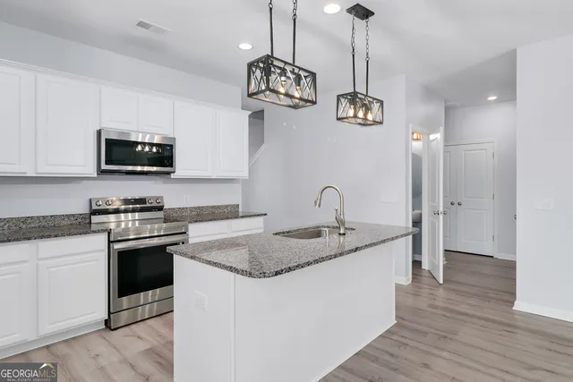 a kitchen with stainless steel appliances granite countertop a stove a sink dishwasher and a microwave oven with white cabinets