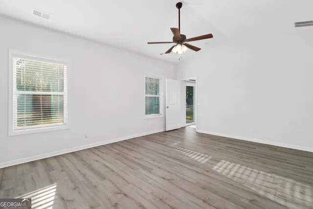 a view of empty room with wooden floor fan and window