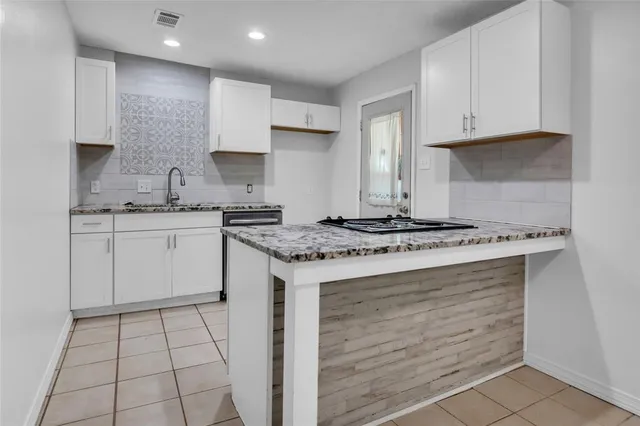 a kitchen with granite countertop a stove a sink and white cabinets