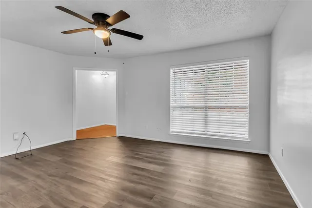 an empty room with wooden floor chandelier fan and windows