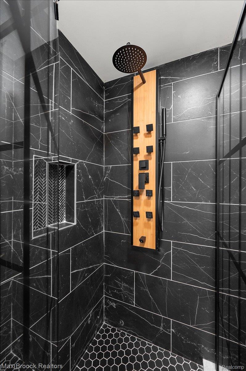 4597 Clarkston Road Clarkston, MI 48348 - Photo 47 of 74 Shower featuring black marble-look wall tiles, black hexagonal floor tiles, a built-in niche with herringbone tile, and a multi-function shower panel with a rain shower head