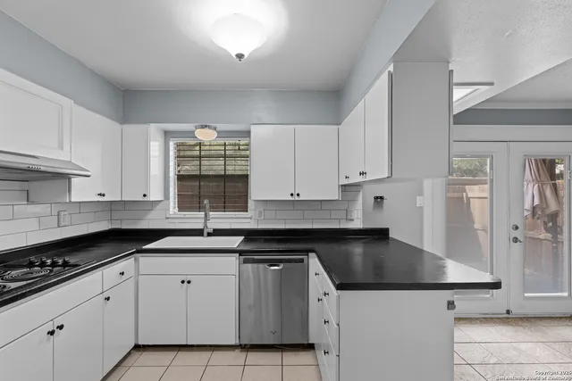 a kitchen with a sink dishwasher a stove and white cabinets