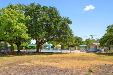 9906 Parliament House Road Austin, TX 78729 - Photo 28 of 33 Picture from backyard of Mature trees shade a fenced community swimming pool area bordering an open grassy space.