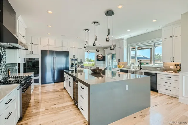 a large kitchen with stainless steel appliances kitchen island granite countertop a large counter top a stove a chimney a sink and a refrigerator