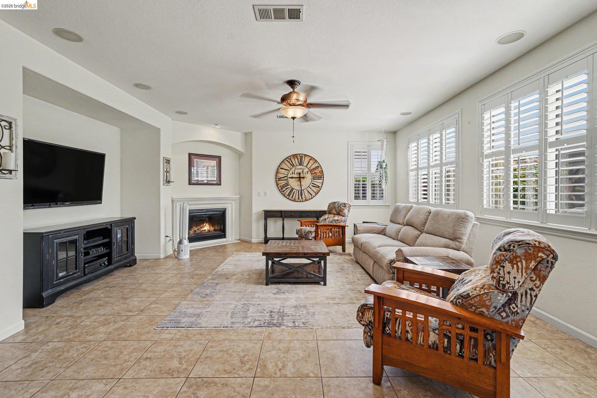 106 Little Ranch Circle Oakley, CA 94561 - Photo 11 of 34 Spacious living area featuring tile flooring, a corner fireplace with mantel, multiple windows with plantation shutters, a ceiling fan, and built-in ceiling speakers