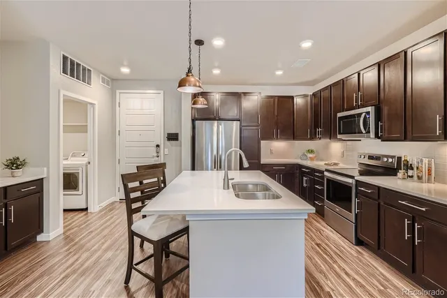 a kitchen with stainless steel appliances kitchen island granite countertop a stove top oven a sink dishwasher a dining table and chairs with wooden floor