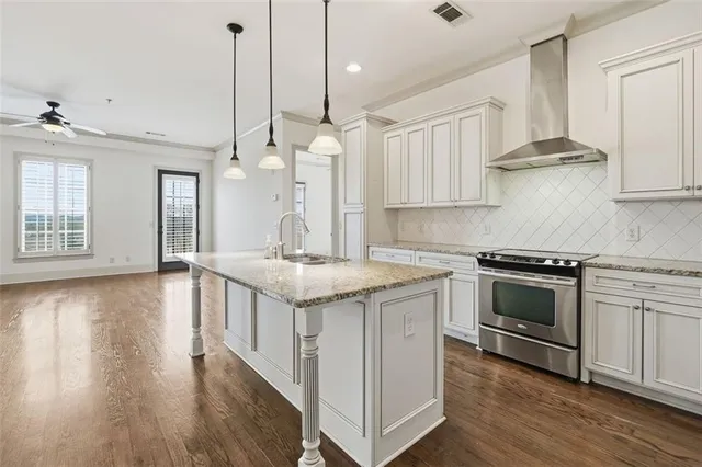 a kitchen with stainless steel appliances granite countertop a sink a stove and white cabinets with wooden floor