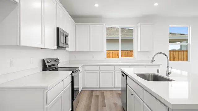 a kitchen with stainless steel appliances granite countertop a sink a stove and white cabinets with wooden floor