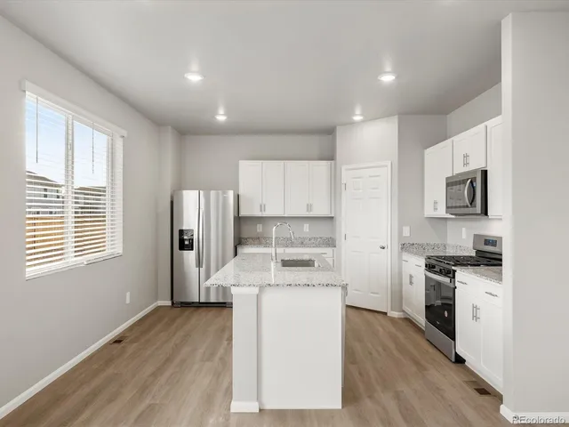 a kitchen with stainless steel appliances granite countertop a stove top oven a sink a refrigerator white cabinets and wooden floor