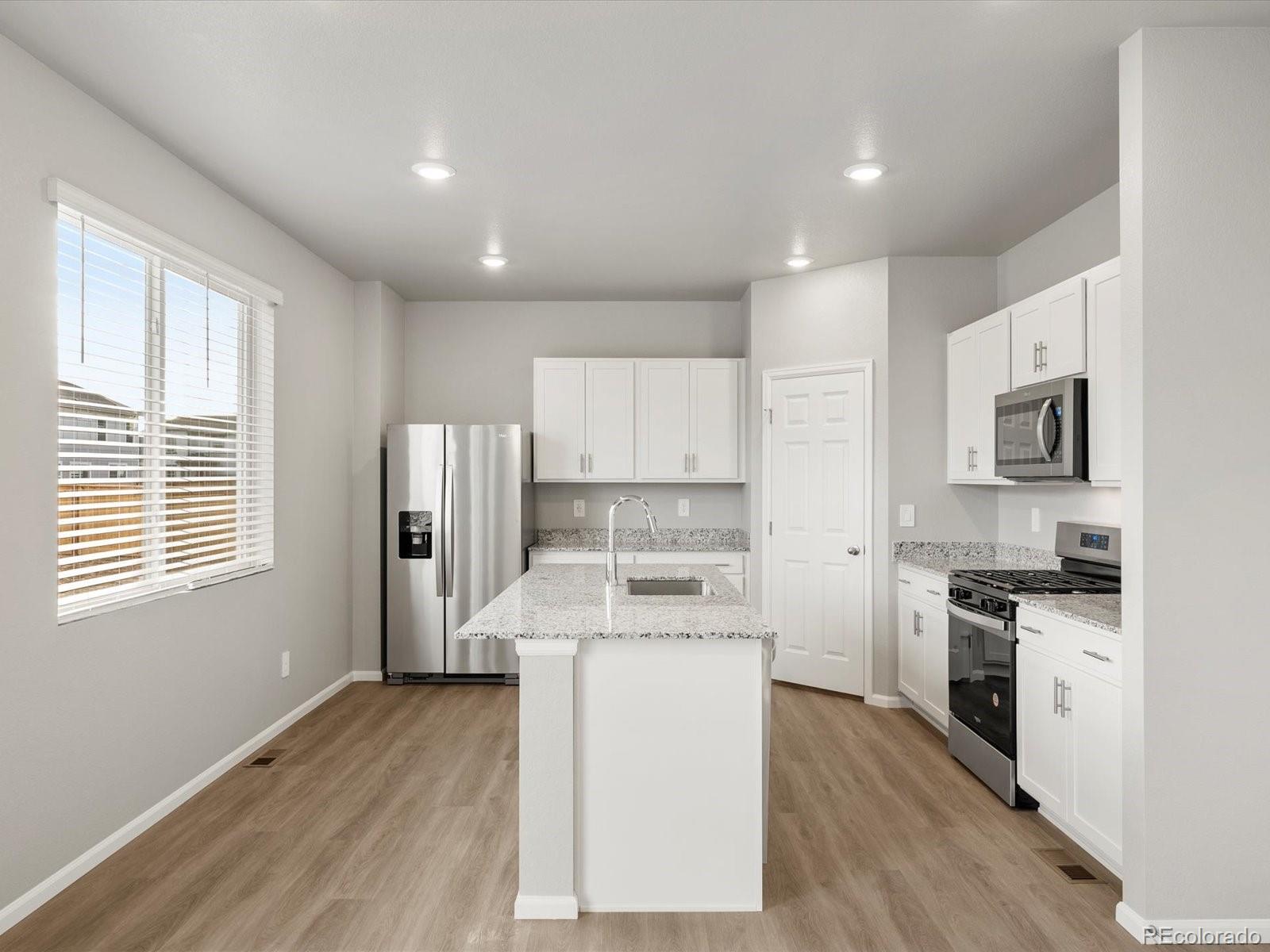 4674 Rabbitbrush Street Johnstown, CO 80534 - Photo 10 of 29 a kitchen with stainless steel appliances granite countertop a stove top oven a sink a refrigerator white cabinets and wooden floor