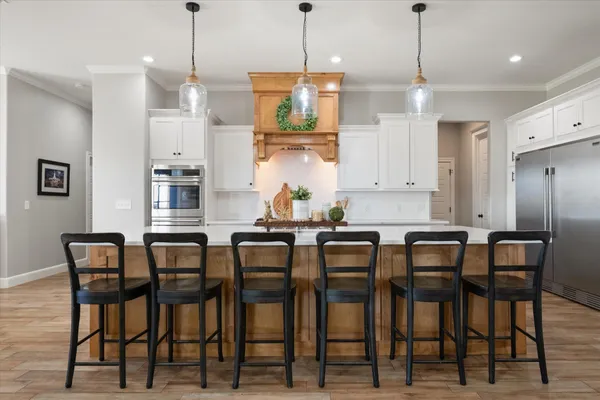 a large kitchen with stainless steel appliances kitchen island granite countertop a stove a sink a refrigerator and white cabinets with wooden floor