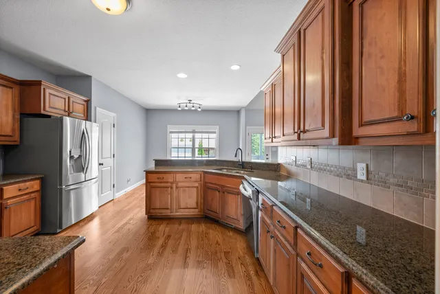 a kitchen with stainless steel appliances granite countertop a refrigerator a sink dishwasher a stove with wooden cabinets and floor