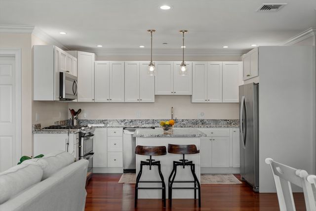 a kitchen with stainless steel appliances granite countertop a stove a refrigerator a white table and chairs with wooden floor