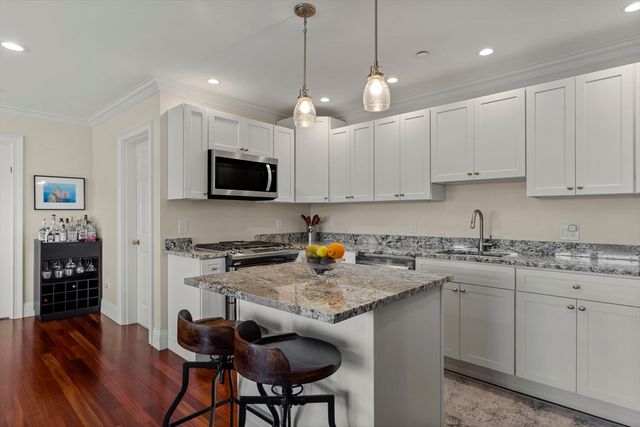 a kitchen with stainless steel appliances granite countertop a stove top oven a sink a refrigerator a dining table and chairs with wooden floor