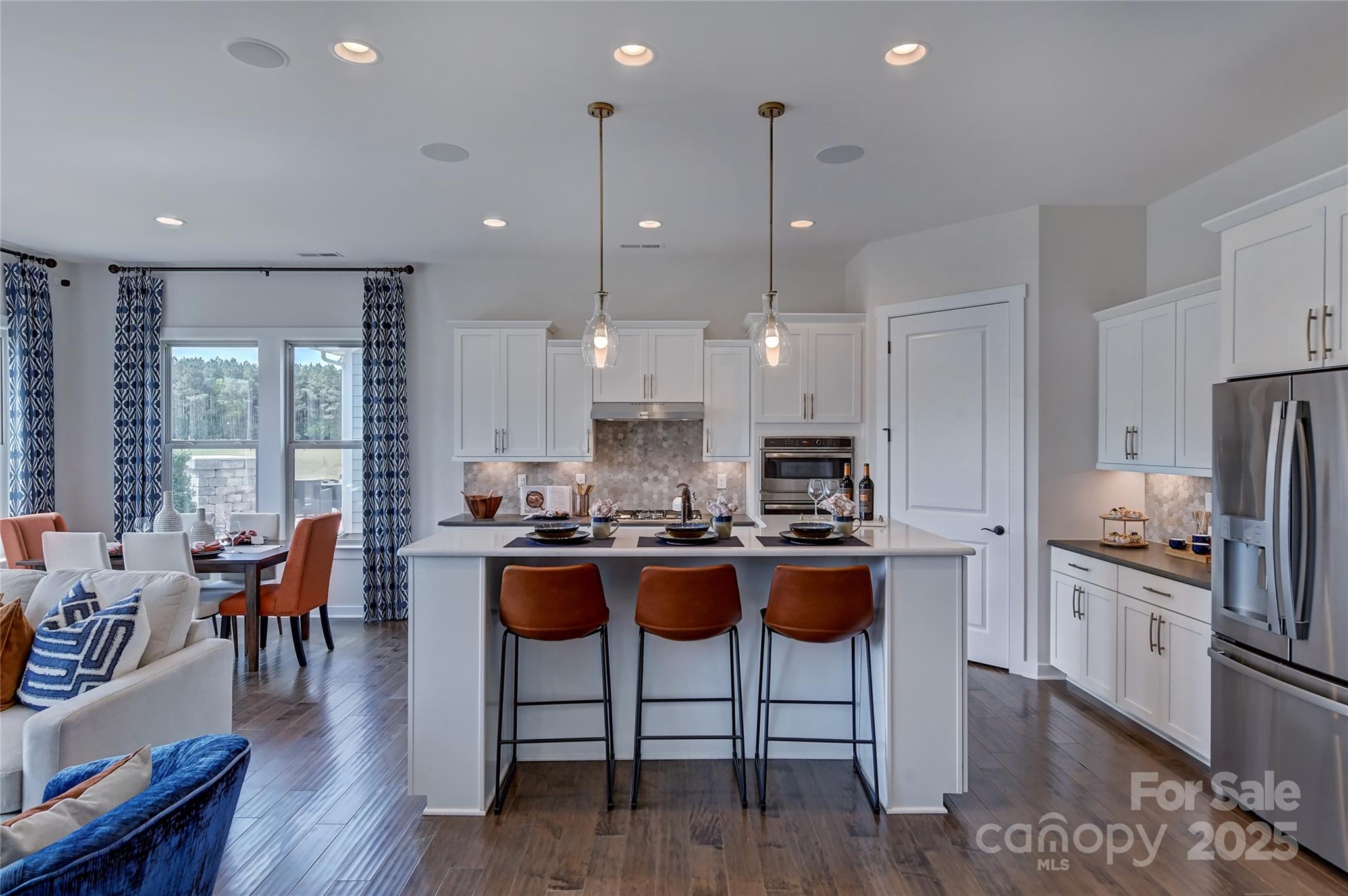 1475 Hubert Graham Way Tega Cay, SC 29708 - Photo 6 of 27 a kitchen with stainless steel appliances granite countertop a stove a refrigerator a kitchen island a dining table and chairs with wooden floor