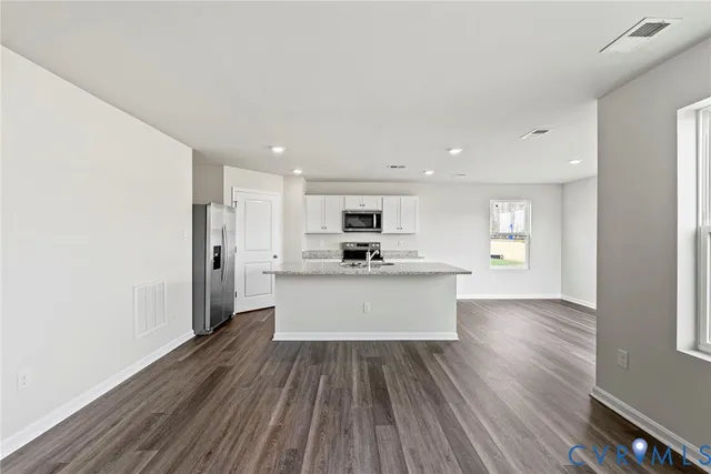 a large kitchen with stainless steel appliances kitchen island a sink dishwasher a refrigerator and white cabinets with wooden floor