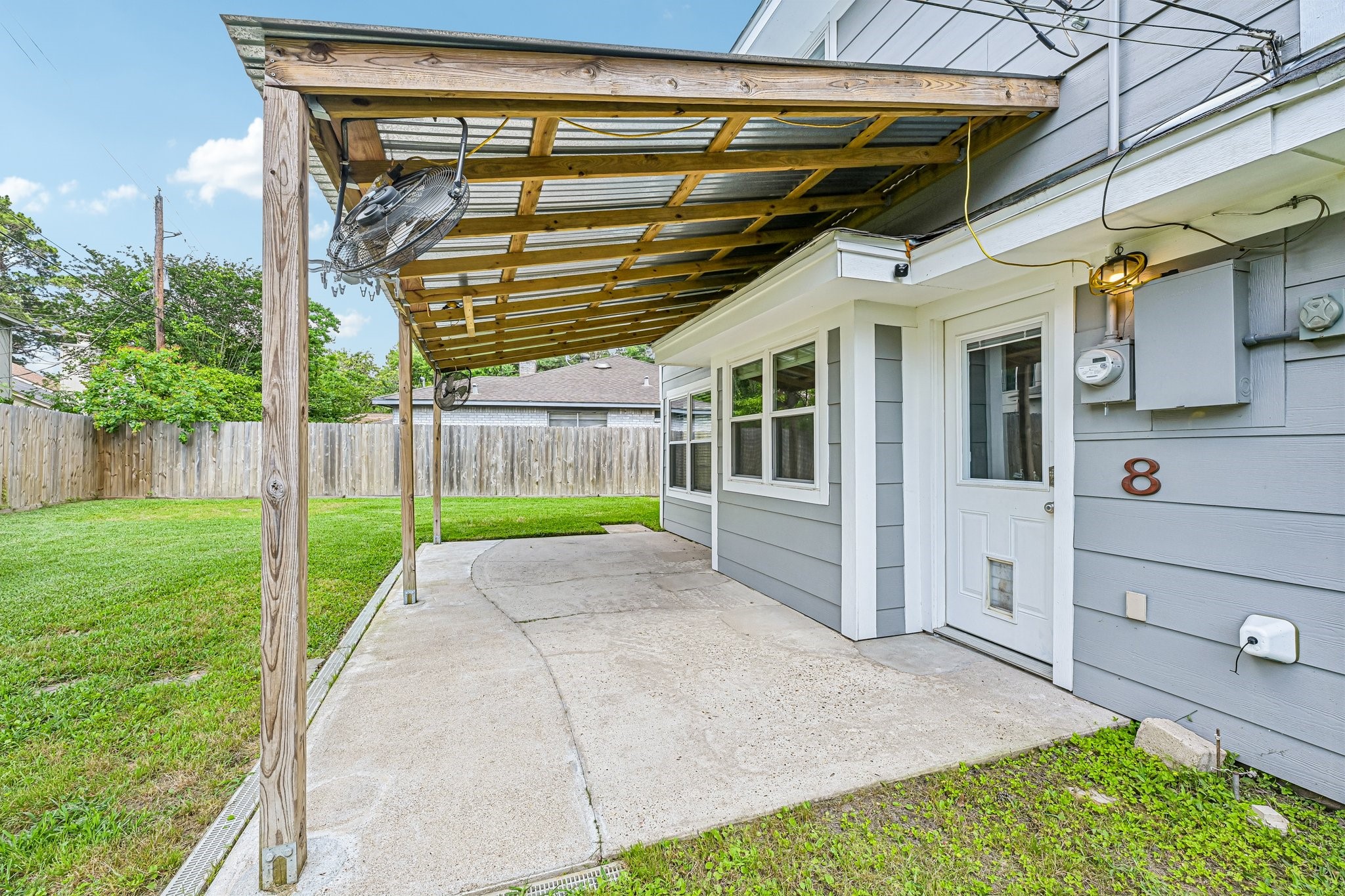 8 Arlington Street Conroe, TX 77301 - Photo 33 of 37 This photo showcases the backyard patio area featuring a covered wooden pergola. The space has a concrete floor, two ceiling fans and a fenced grassy yard, providing a cozy outdoor setting.