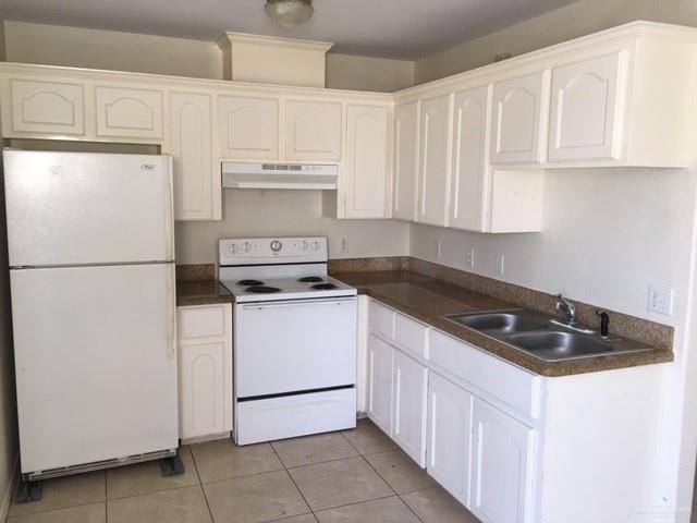 401 Rockport Street Alton, TX 78573 - Photo 7 of 11 Kitchen with white appliances, dark countertops, under cabinet range hood, light tile patterned floors, and white cabinetry