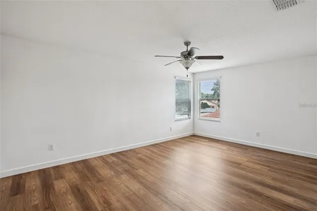 an empty room with wooden floor chandelier fan and windows