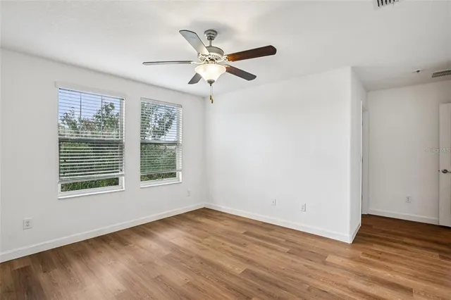 an empty room with wooden floor fan and windows