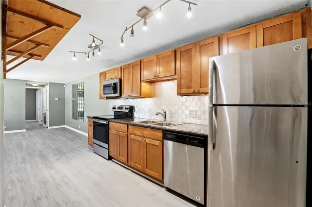 a kitchen with stainless steel appliances granite countertop a refrigerator a sink dishwasher a stove with white cabinets and wooden floor