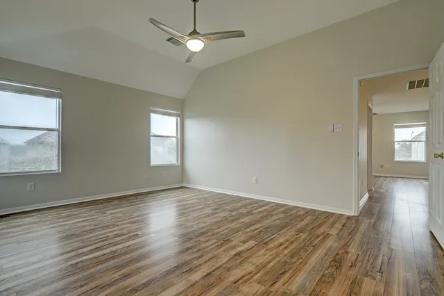 an empty room with wooden floor ceiling fan and windows