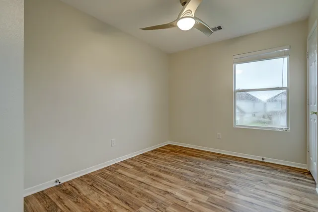 an empty room with wooden floor chandelier fan and windows