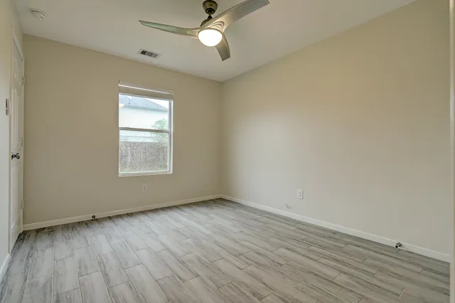 an empty room with wooden floor fan and windows