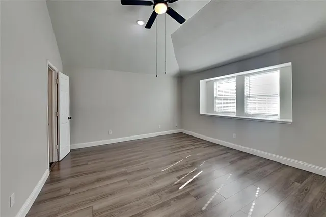an empty room with wooden floor ceiling fan and windows