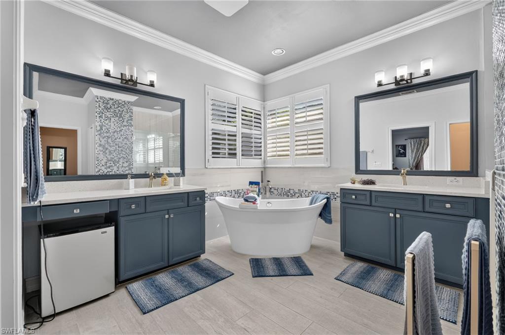 9970 Rookery Circle Estero, FL 33928 - Photo 35 of 50 Freestanding soaking tub with mosaic tile surround, dual vanities featuring custom cabinetry, framed mirrors with integrated lighting, and plantation shutters