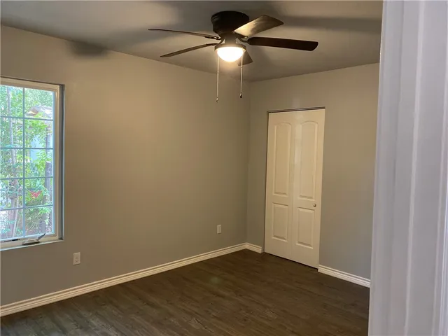 an empty room with wooden floor chandelier fan and windows