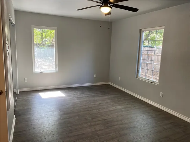 an empty room with wooden floor fan and windows