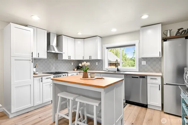 a kitchen with stainless steel appliances granite countertop a refrigerator a sink dishwasher a stove and white countertops with wooden floor