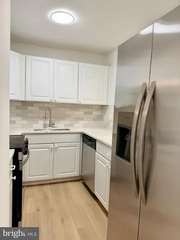 a kitchen with stainless steel appliances granite countertop a refrigerator a sink and white cabinets