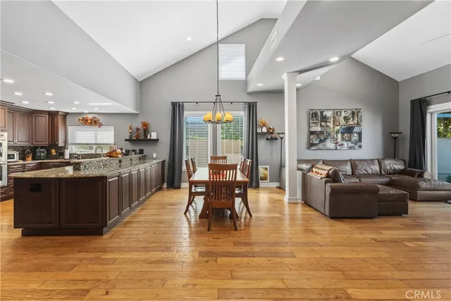 a kitchen with stainless steel appliances kitchen island granite countertop a refrigerator a stove top oven and a dining table with wooden floor