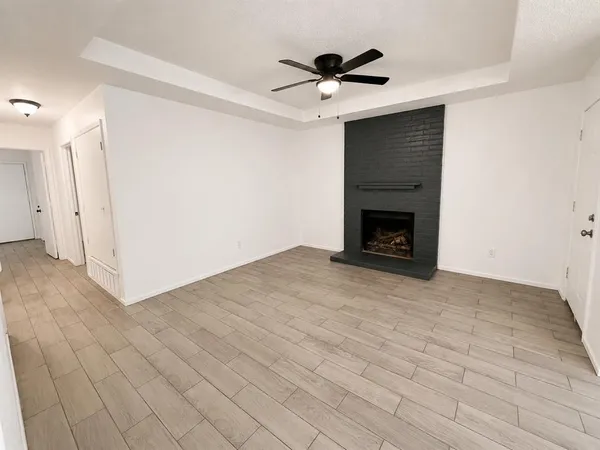 a view of an empty room with wooden floor a fireplace and a window