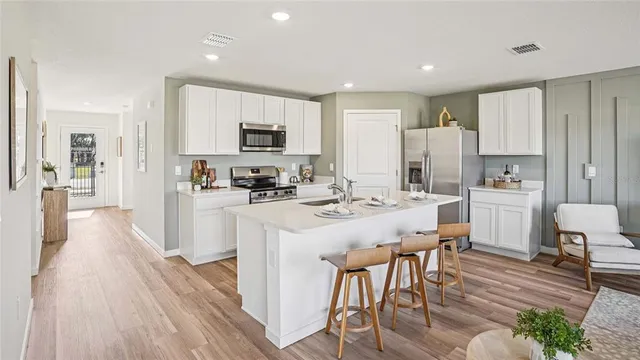 a kitchen with stainless steel appliances a microwave a stove a refrigerator a sink a dining table and chairs with wooden floor