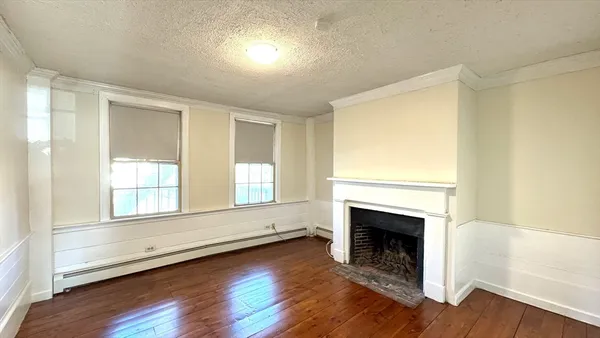an empty room with wooden floor fireplace and windows
