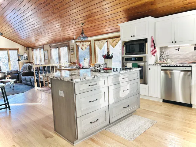 a kitchen with stainless steel appliances kitchen island granite countertop a refrigerator a stove a sink dishwasher and white cabinets with wooden floor