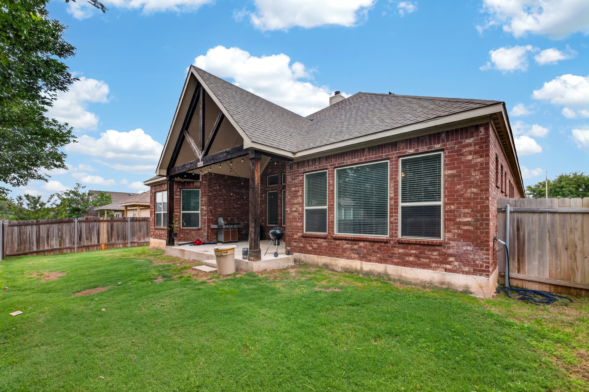 1017 Tabernash Leander, TX 78641 - Photo 35 of 38 Rear exterior featuring a brick facade, covered patio with wood beam accents, and a spacious grassy yard