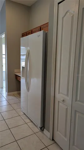 a view of a refrigerator in kitchen and an empty room in wooden floor