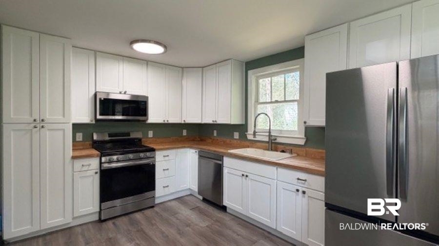 Kitchen with stainless steel appliances, white cabinetry, and dark wood-type flooring