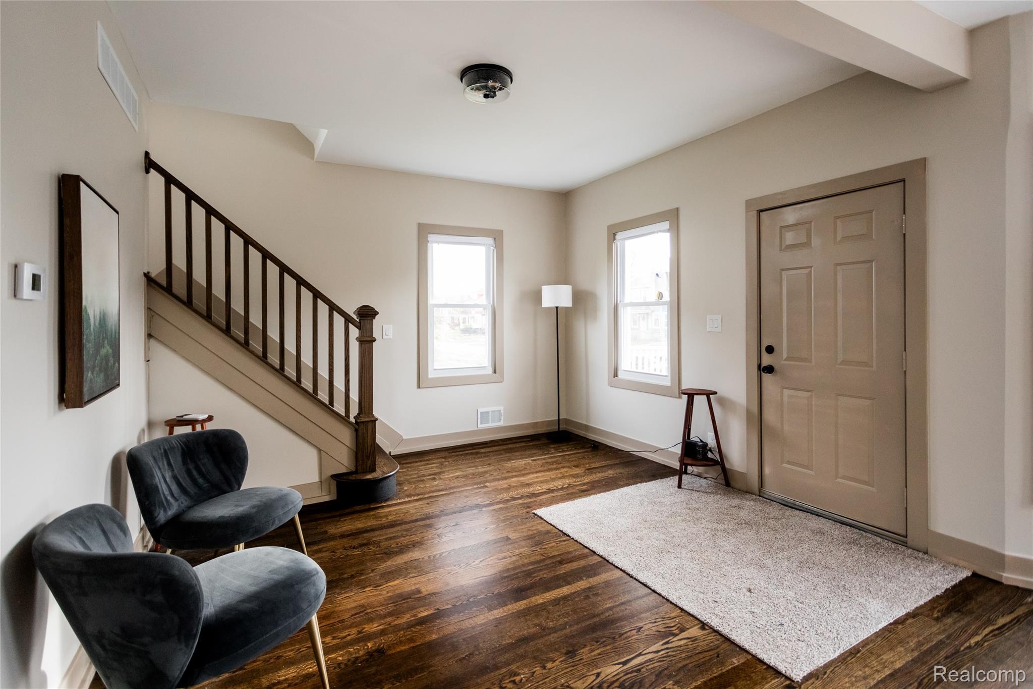 2630 Harding Street Detroit, MI 48214 - Photo 4 of 30 Entryway featuring rich wood-finish flooring, a paneled entry door, two windows with trim, a staircase with wooden newel post and balusters, and a ceiling-mounted light fixture