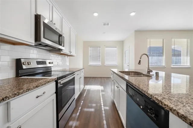 a kitchen with granite countertop stainless steel appliances a sink dishwasher a stove top oven a refrigerator with wooden cabinets and floor