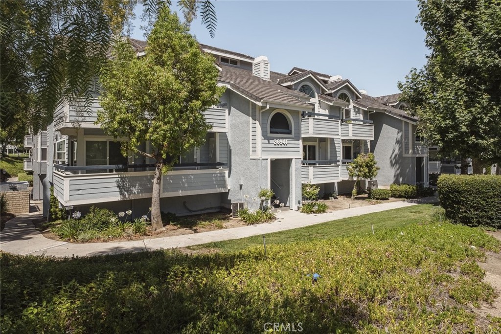26941 Rainbow Glen Drive, Unit 751 Santa Clarita, CA 91351 - Photo 27 of 34 a view of a white house with a yard and lawn chairs under a large tree