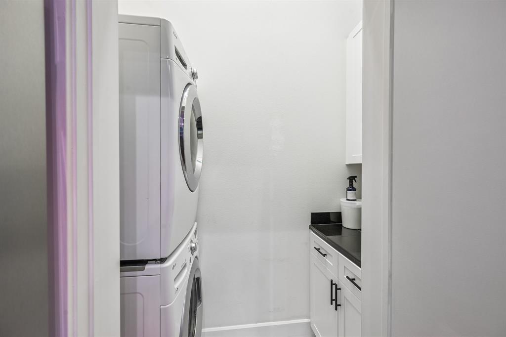 3553 Wheeler Street Dallas, TX 75209 - Photo 20 of 35 Laundry room with stacked washer and dryer, white cabinetry, and black granite countertop