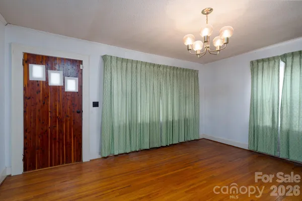 an empty room with wooden floor chandelier and windows