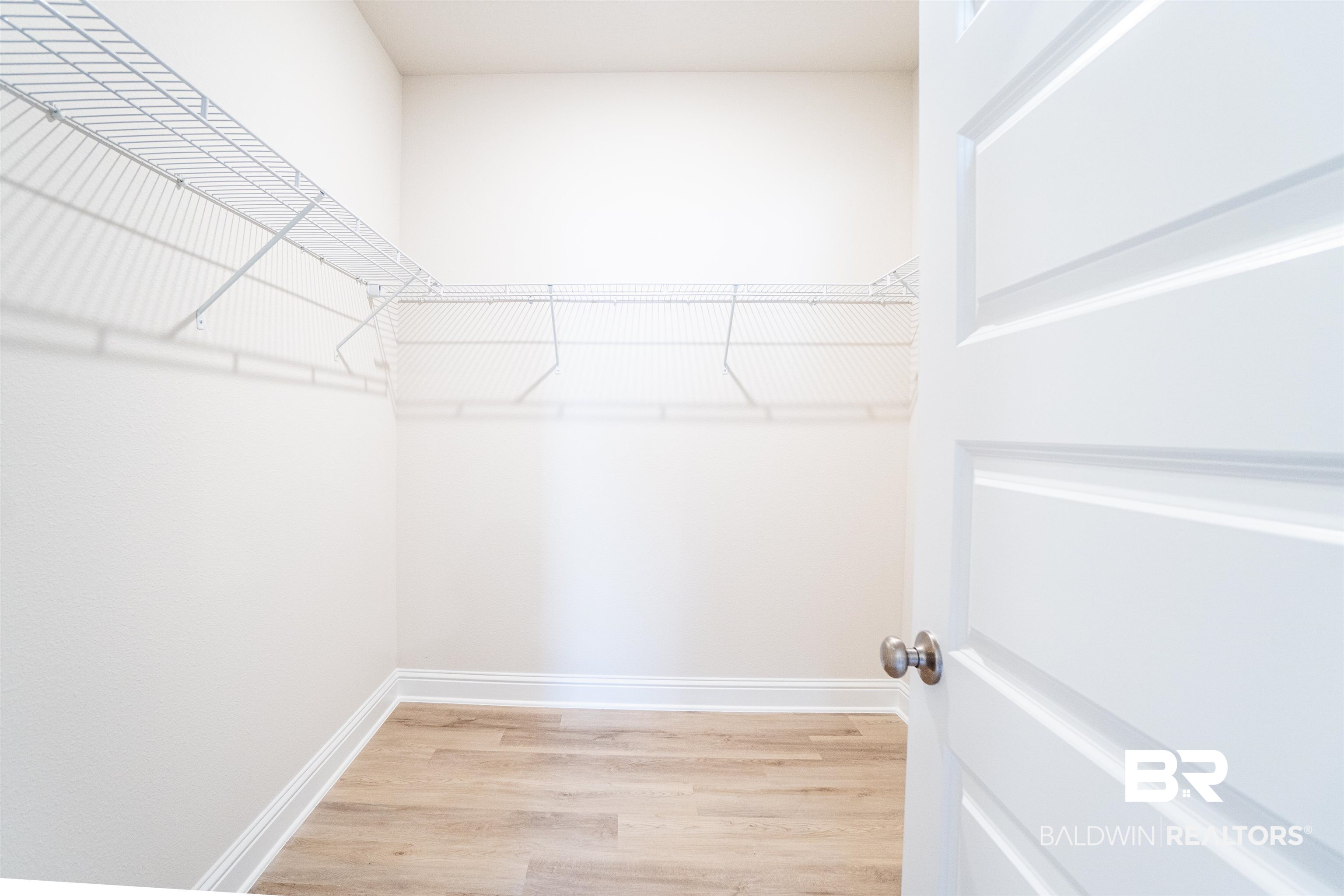 1073 Hayward Loop Foley, AL 36535 - Photo 12 of 18 Walk-in closet featuring wire shelving, light wood-finish flooring, white baseboards, and a paneled door with a brushed nickel knob