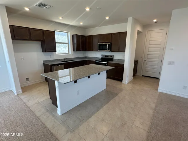 a large kitchen with stainless steel appliances kitchen island granite countertop a refrigerator and a stove top oven