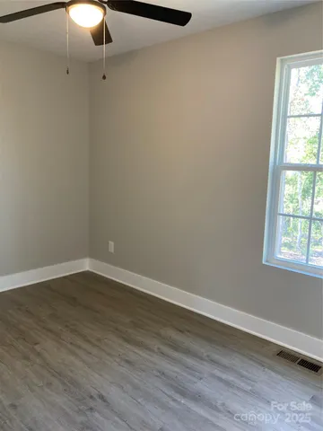 an empty room with wooden floor fan and windows